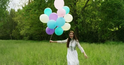 Joyful Woman Twirling with Balloons in Grassy Field