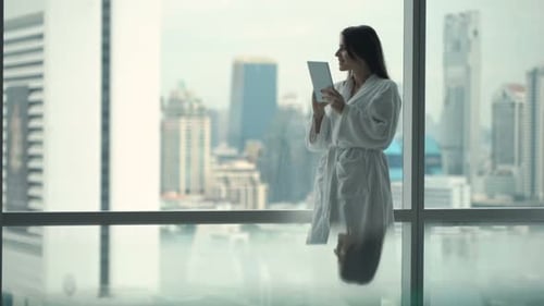 Woman in Robe Using Tablet with City View