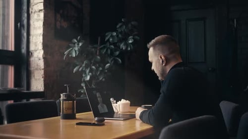 Ein junger Mann in einem Café mit einem Laptop kommuniziert per Video mit seinem Patienten, einem freiberuflichen Psychologen