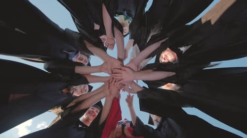 Recent Graduates in Cap and Gown Join Hands in a Circle