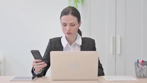 Professional Woman Works at Desk with Phone and Laptop