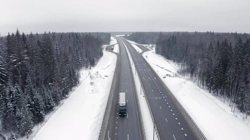 a highway in the middle of a snow-covered forest with a black and silver car