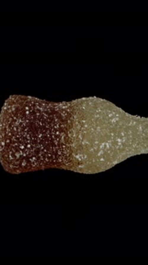 Vertical video. Gummy candy in the shape of a cola bottle, rotating on a black background, isolated.