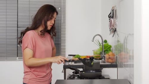 Woman Cooking Food in Frying Pan in Kitchen
