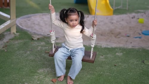 slow motion of cheerful child girl playing on wooden swing at playground