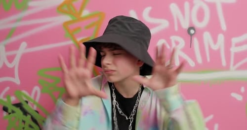Teen in Bucket Hat Gesturing in Front of Graffiti