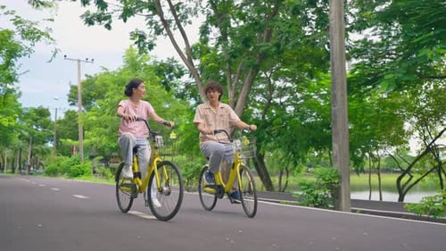 Asian young couple dating and biking together on a road in the park.