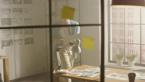 Creative Designer Walks around His Studio, Sits on His Desk Holds Laptop on the Knees while Working