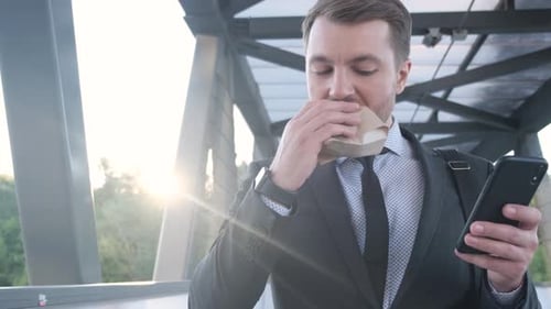 Man in Suit Eats Burger While Using Phone