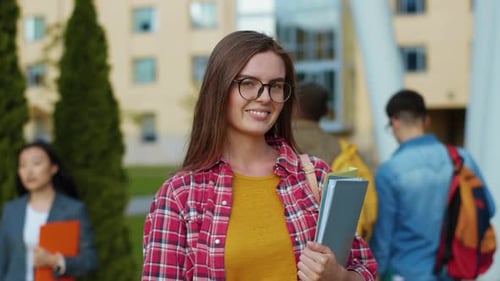 Attractive Brunette Young Woman with Books Standing at a University Portrait Face of Stylish College