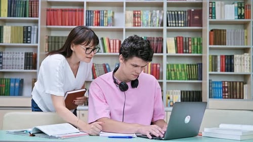 Woman Mentor Teaching Male Student in College Library Exam Preparation