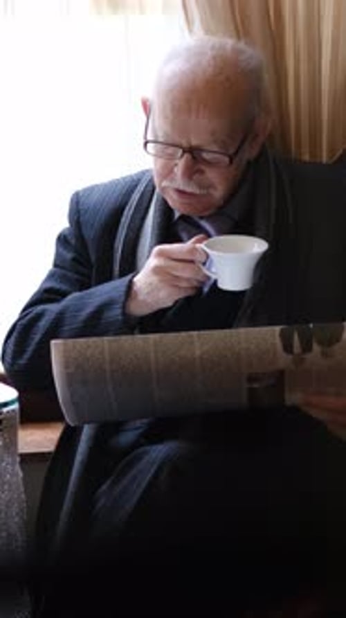 Elderly Man Cautiously Enjoying His Morning Cup of Coffee While Reading the Daily Newspaper