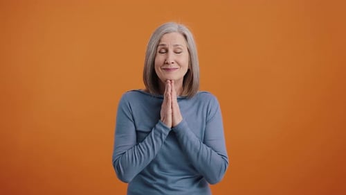 Mature Woman Clasping Hands on Orange Background
