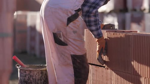 bricklaying worker in a sunny cinematic scenic handheld shot, creating insulating walls