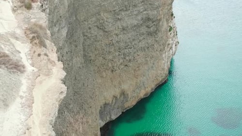 Woman Standing On The Edge Of Island Cliff Admiring The Calm Blue Waters Of Sea. - high angle, revea