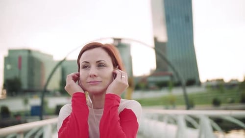 Young Woman with Earphones on Bridge Outdoors in City, Resting After Exercise