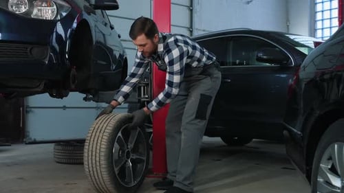 View from the side, moving tire. Man is repairing the car at a service station