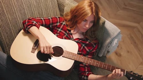 Woman with Red Hair Plays Guitar on Sofa