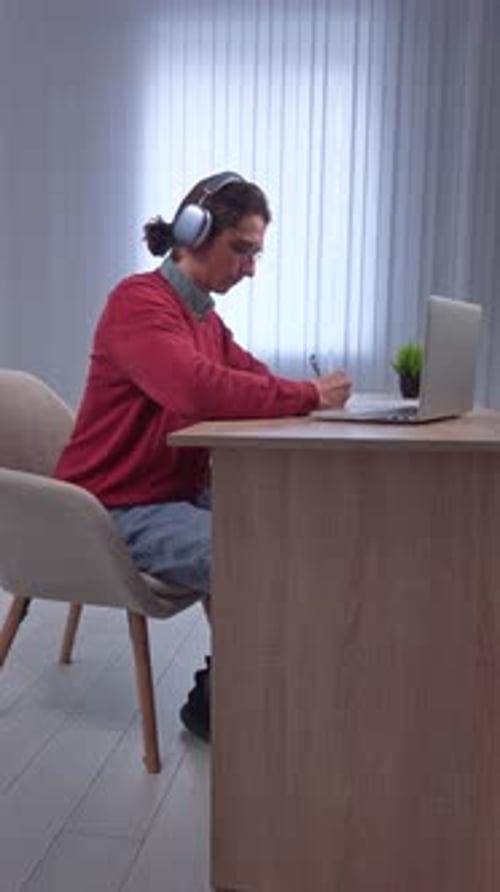 Young Adult Man Spending Time at Home Man Student Sits at Desk Works on Computer Finishing Studying