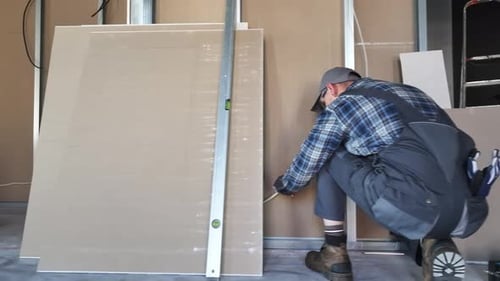 Construction Worker Measuring Drywall with Level Indoors