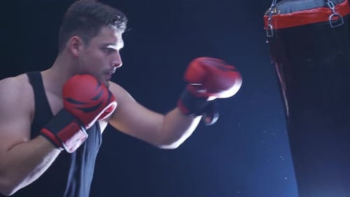 Strong athlete punches punching bag in dusty gym. Cinematic boxing scene.