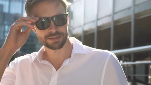 Smiling Man Adjusts Sunglasses on Sunny City Street