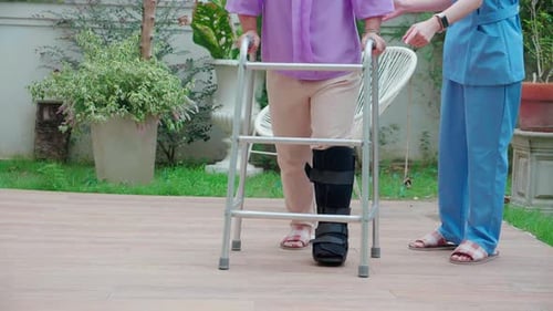 Senior Woman Using Walker Assisted by Caregiver