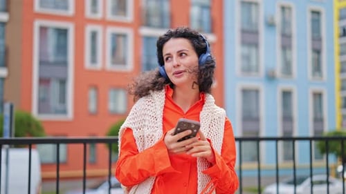 Happy Woman Listening to Music On Headphones and Using Phone in City