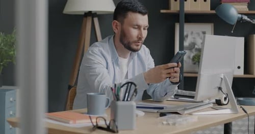 Junger Unternehmer surft auf dem Smartphone und schreibt dann Informationen in ein Notizbuch und arbeitet am Schreibtisch