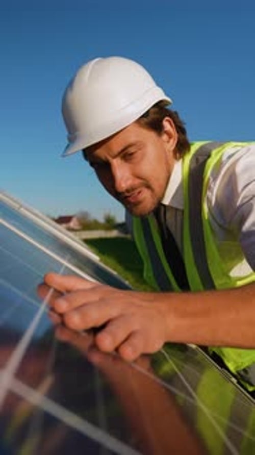 An Engineer in a Safety Vest and Helmet Carefully Examines the Surface of a Solar Panel