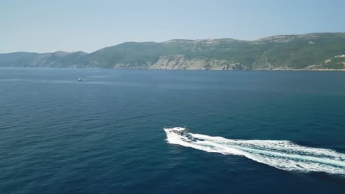 Boat speeding through clear blue sea near rugged coastline, aerial view