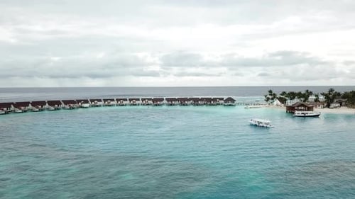 Foto de drone de vilas aquáticas, iates e uma ilha com palmeiras em um resort nas Maldivas. Azul e turquesa