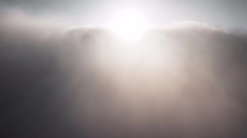 Vista aérea volando a través de una espesa capa de nubes, puesta de sol detrás de las nubes