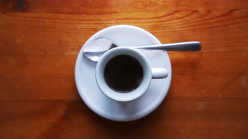 Aufnahme einer heißen Espressotasse mit Teller und Löffel. Stehend auf einem braunen Holztisch. Steam ist ein Risiko