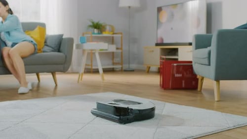 Close Up Shot of a Smart Robot Vacuum Cleaner Sucking Up Dust from a Carpet. Beautiful Couple is Si
