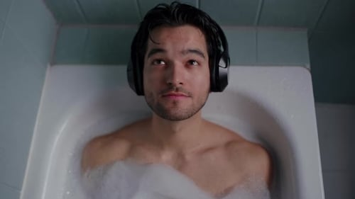 Top View Of A Man Relaxing In The Bathtub With Music On His Ears