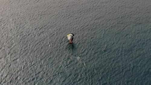 drone shot of man doing windsurfing in the sea.