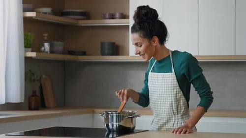 Woman Smiling Stirs Pot in Modern Kitchen
