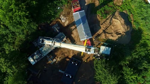 A large crane on a construction site surrounded by trees and in daylight, aerial view