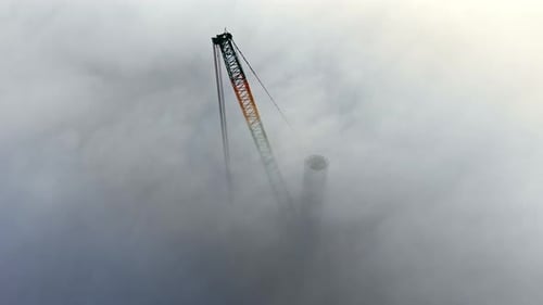 Smokestack Shrouded in Dense Fog Above Construction Tower Project
