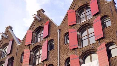Dynamic moving shot of three traditional historic Amsterdam brick houses with red wooden shutters on