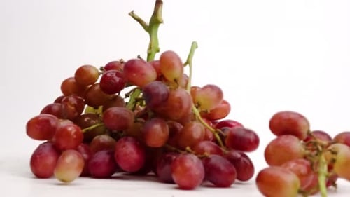 Saftige rote Weintrauben am Weinstock, die in Zeitlupe auf einer weißen Tischplatte zu einem Haufen fallen