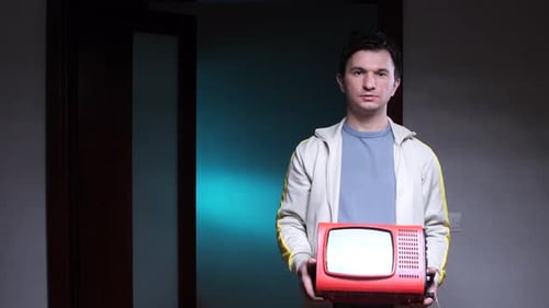 Mann hält tragbaren Fernseher in der Hand, alter alter Retro-Fernseher, rot, im dunklen Raum