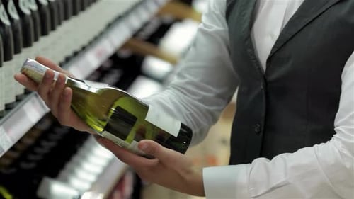 Person Inspecting Wine Bottle in Store