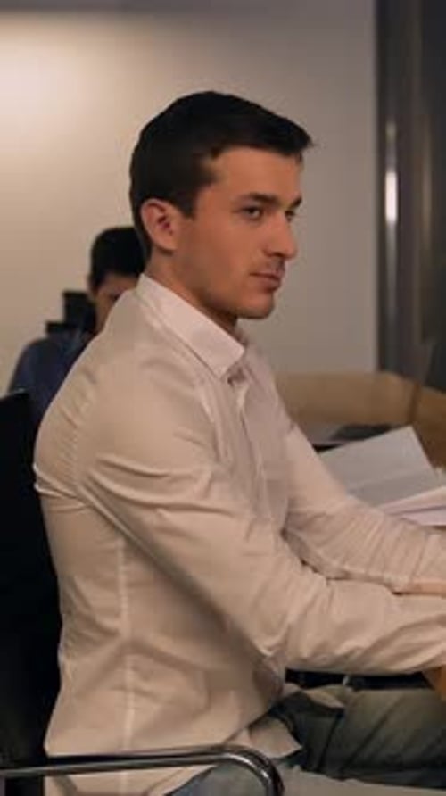 Vertical of Handsome Young Man Writes in a Notebook Looks at the Monitor in Office and Than Look to