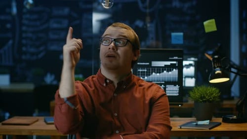 Young Office Worker Has Eureka Moment While Sitting in His Office Thinking, Bulb Over Him Lights Up