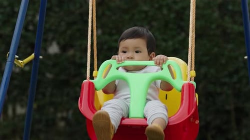 slow-motion of happy infant baby is playing in a swing in the garden