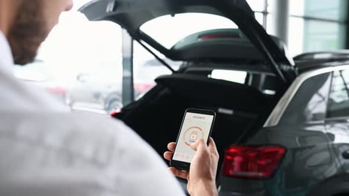 Rear view of man that closing car's trunk by smartphone