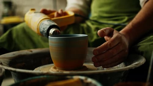 Un potier travaille dans un atelier de poterie en train de sécher un pot en argile crue à l'aide d'un séchoir électrique