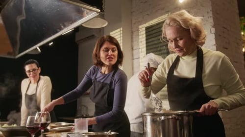 Drei Frauen chatten und kochen mit dem Koch während des Koch-Meisterkurses